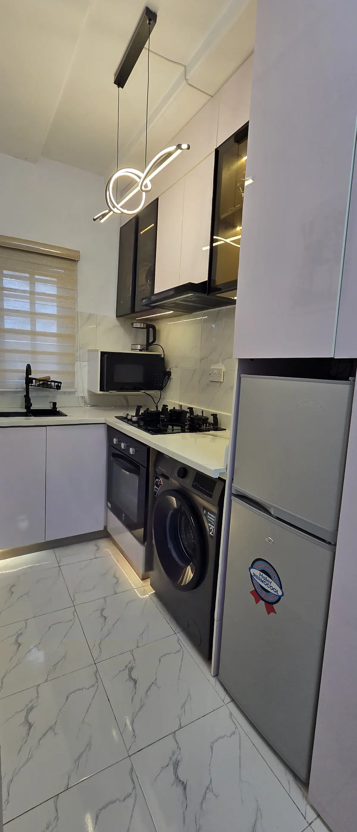 Fitted kitchen with gas hob, oven, washing machine and fridge under a sculptural pendant light