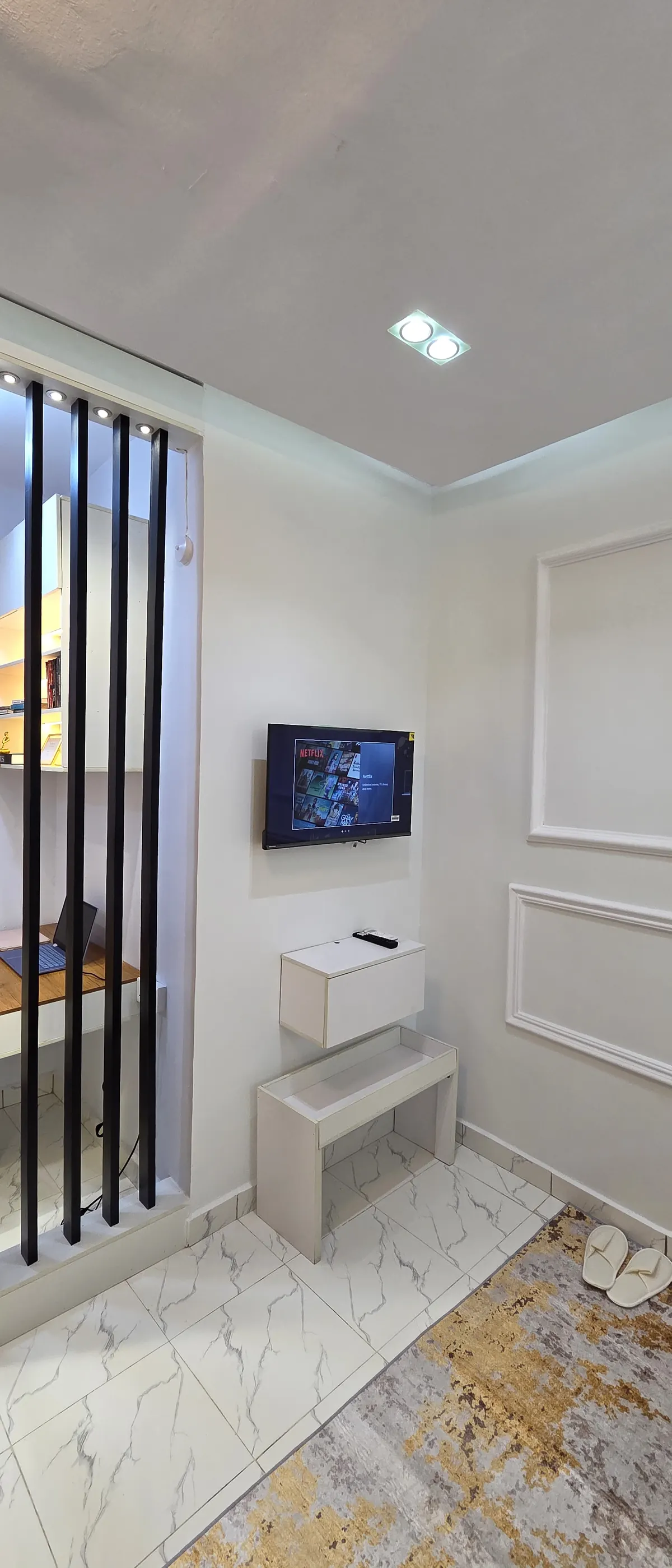 Bright lounge with slatted black partition, wall-mounted TV and marble floor
